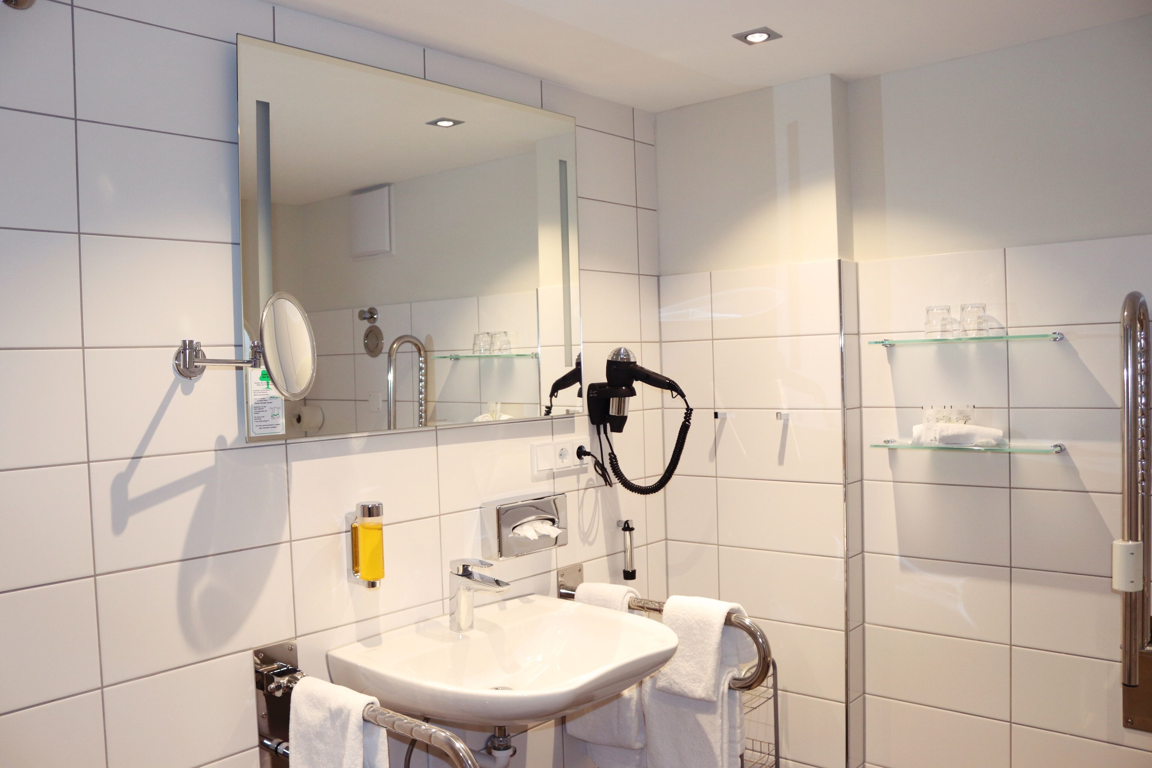 A modern bathroom with a sink, mirror, towel rack, and glass shelves.