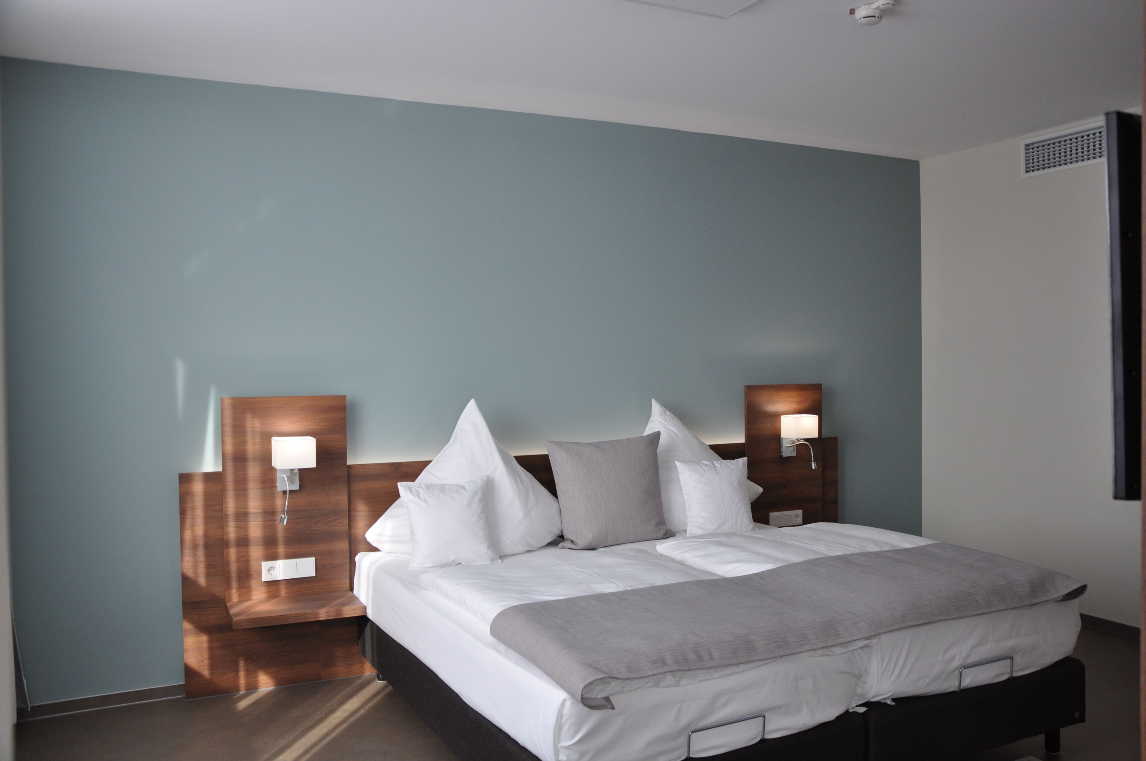 Una habitación de hotel con cama, dos mesitas de noche con lámparas y un aplique de pared.