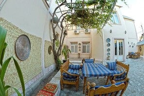 A traditional courtyard with a wooden table and chairs, a woven wall, and a potted plant. - Minzifa Inn (Bukhara)