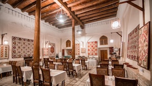 Un comedor espacioso con techos altos de madera y decoraciones murales estampadas. Las mesas están dispuestas con manteles blancos y sillas de madera.
