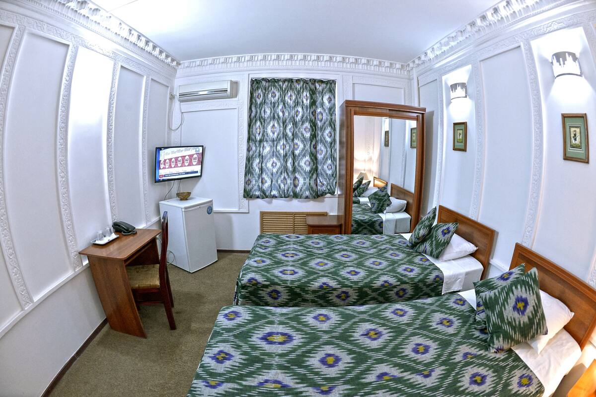 Ein Hotelzimmer mit zwei Betten, einem Schreibtisch, einem Stuhl, einem Fernseher und einem Spiegel.