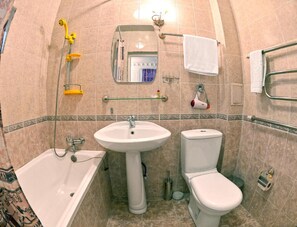A bathroom with a bathtub, sink, toilet, and a shower with yellow fixtures. - Minzifa Inn (Bukhara)