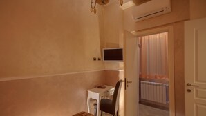 A bedroom with a bed, a desk with a chair, a television, and an air conditioning unit.