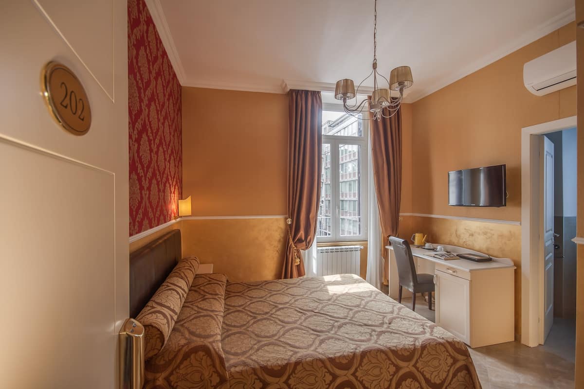 A hotel room with a bed, a desk, a chair, a television, and a window with curtains.