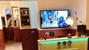 A hotel reception area with a television displaying a movie, a reception desk with illuminated icons, and framed pictures on the wall.
