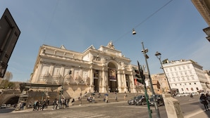 A grand historical building with classical architecture, large steps leading to the entrance, and a busy street in front.