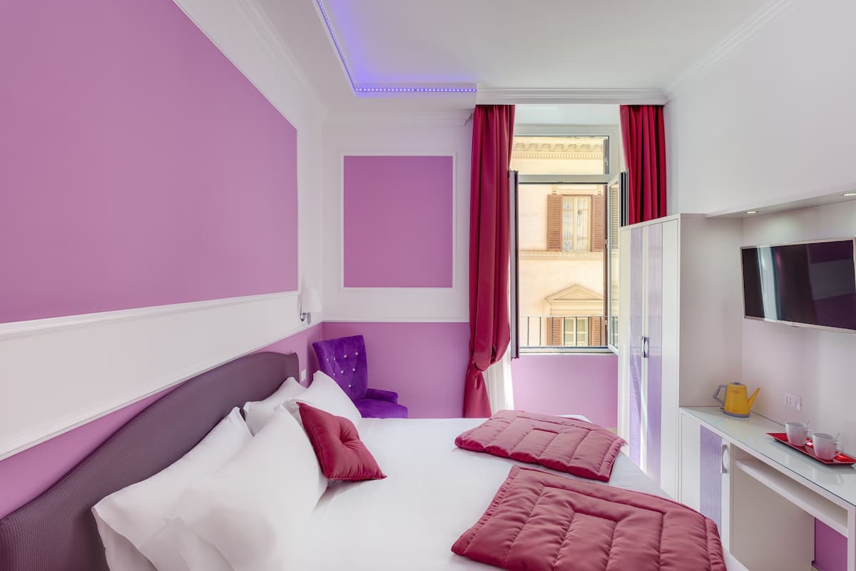 A hotel room with a bed, a desk, a chair, and a TV.