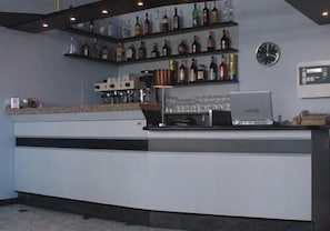 Una zona de bar con estantes llenos de botellas, una máquina de café y un reloj en la pared.