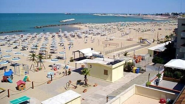Una playa con muchas sombrillas y tumbonas, un parque infantil y un pequeño edificio con el número 3.
