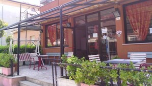 Un espacio al aire libre con mesas y sillas, un porche cubierto y plantas en macetas.