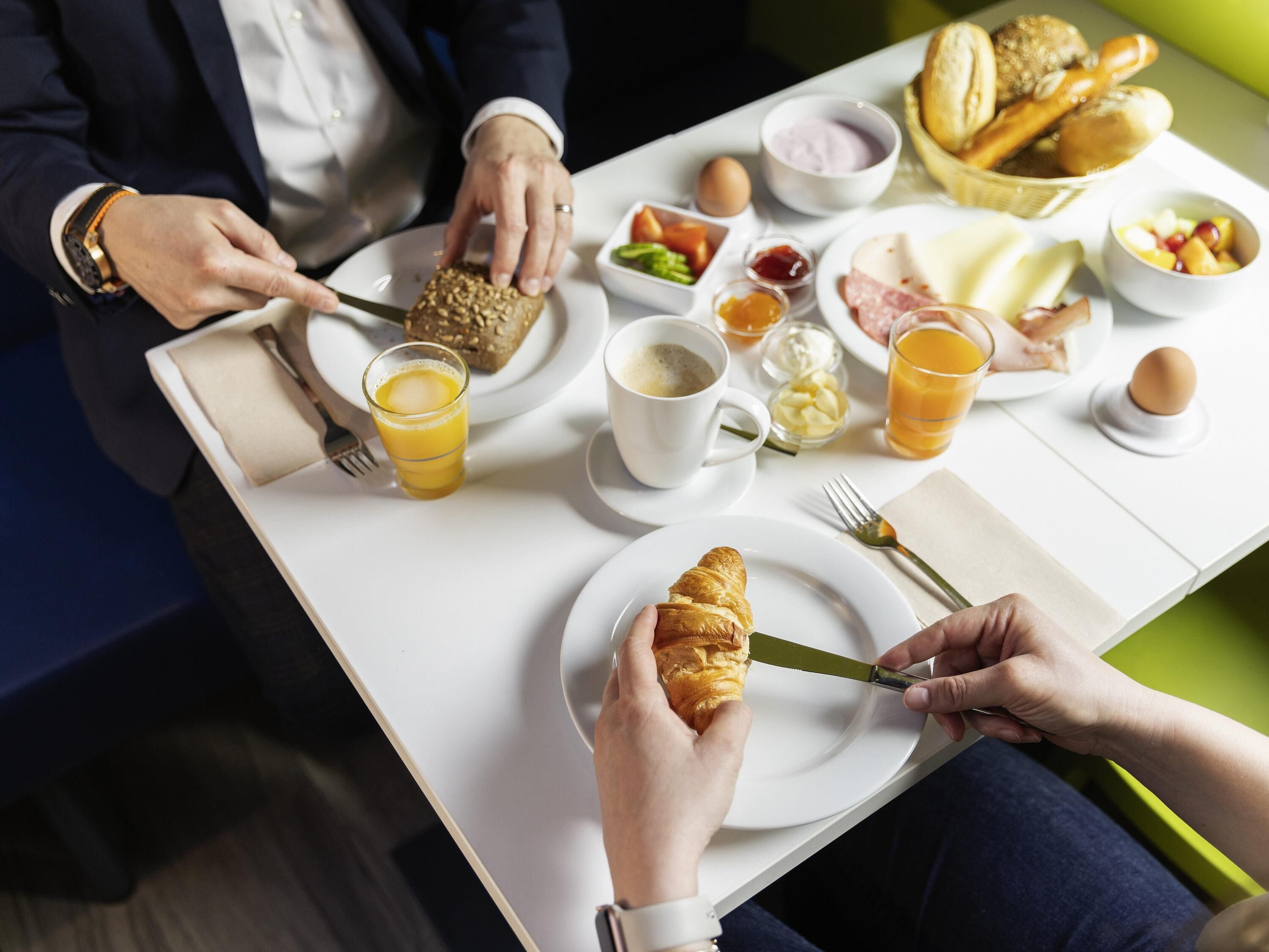 A breakfast table with croissants, eggs, and juice.