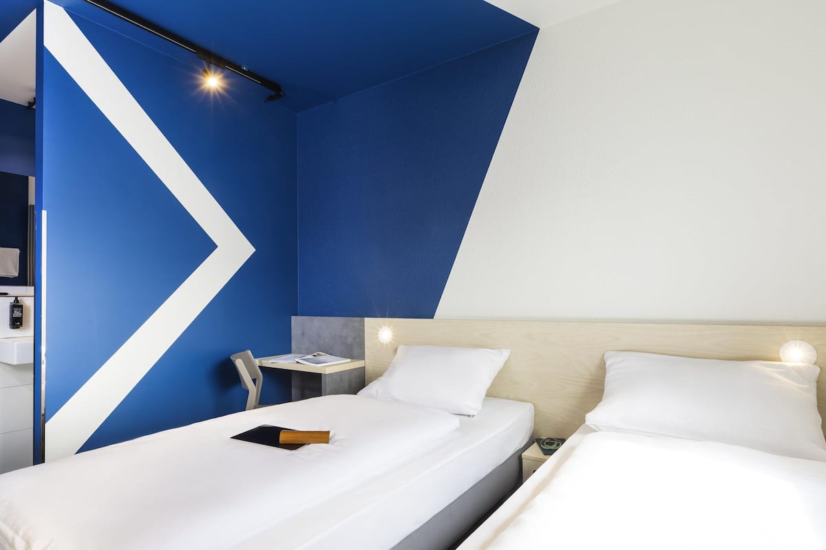 A hotel room with two beds, a desk, and a chair.