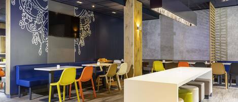 Un interior de restaurante moderno con suelo de madera, sillas coloridas y una mesa blanca en el centro.