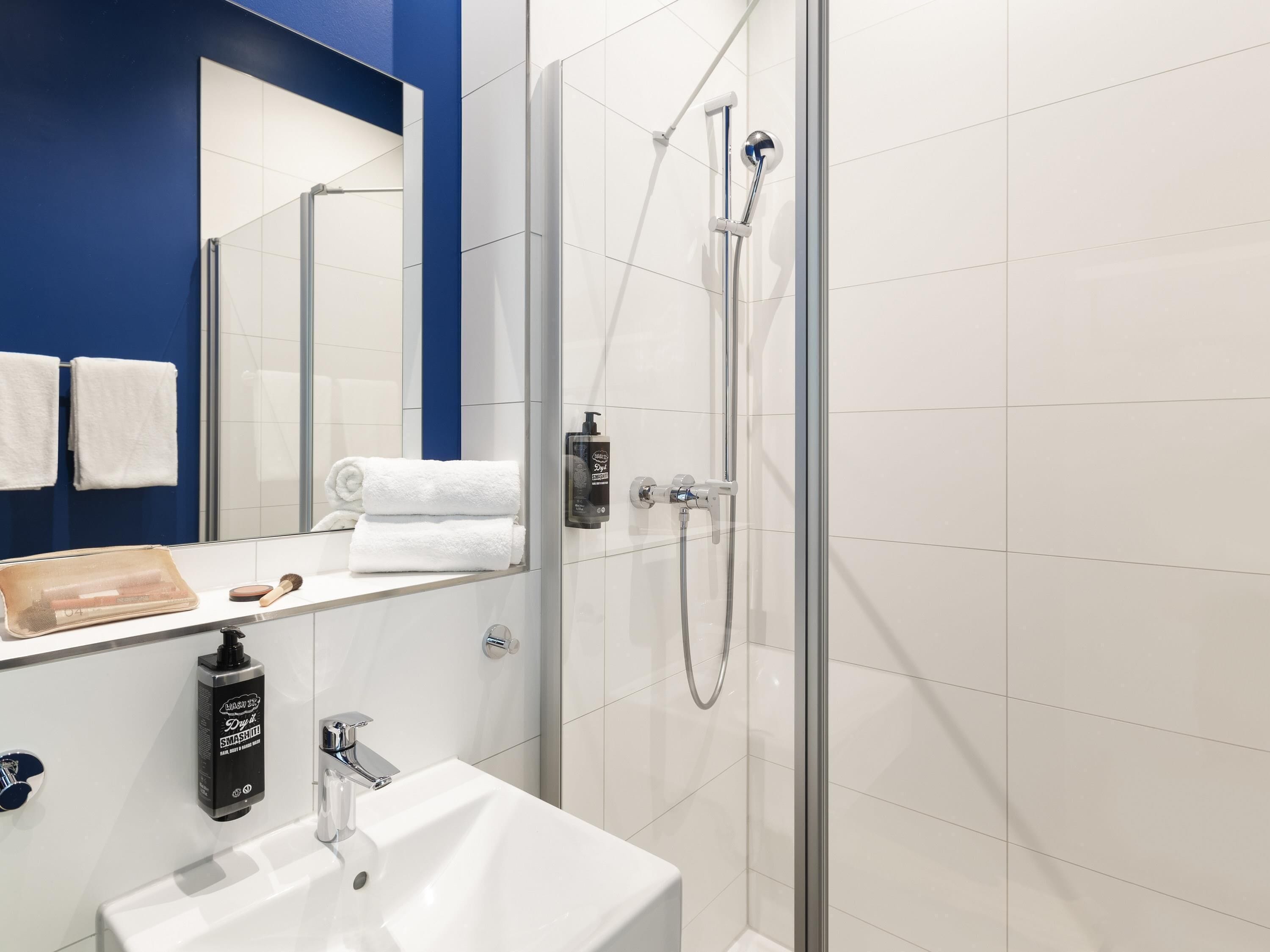 A modern bathroom with a glass shower enclosure, a white sink, a mirror, and neatly folded towels.
