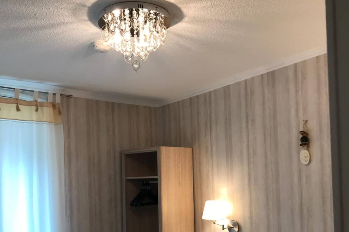 A hotel room with a large bed, a chandelier, a wardrobe, and a bedside table.