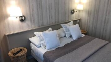 A neatly made bed with a grey blanket and multiple pillows, two wall-mounted lamps, and a woven basket on the floor.
