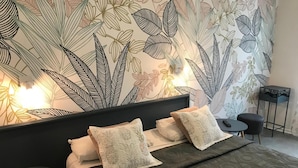 Ein Schlafzimmer mit einem großen Bett, zwei Kissen, einem Nachttisch, einem Sessel und einer Wand mit Blättermotiv.