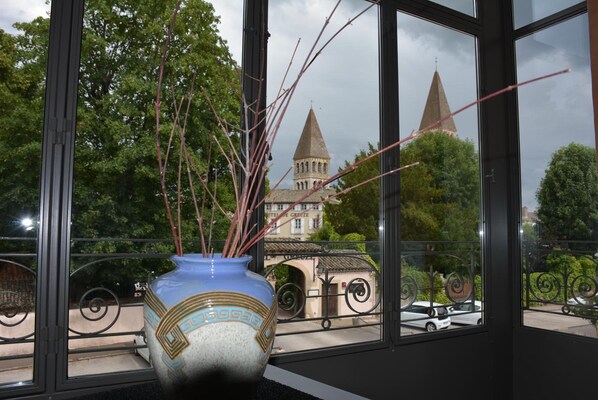 A view through a window with a decorative vase on a windowsill, a balcony railing, and a building with two towers in the background.
