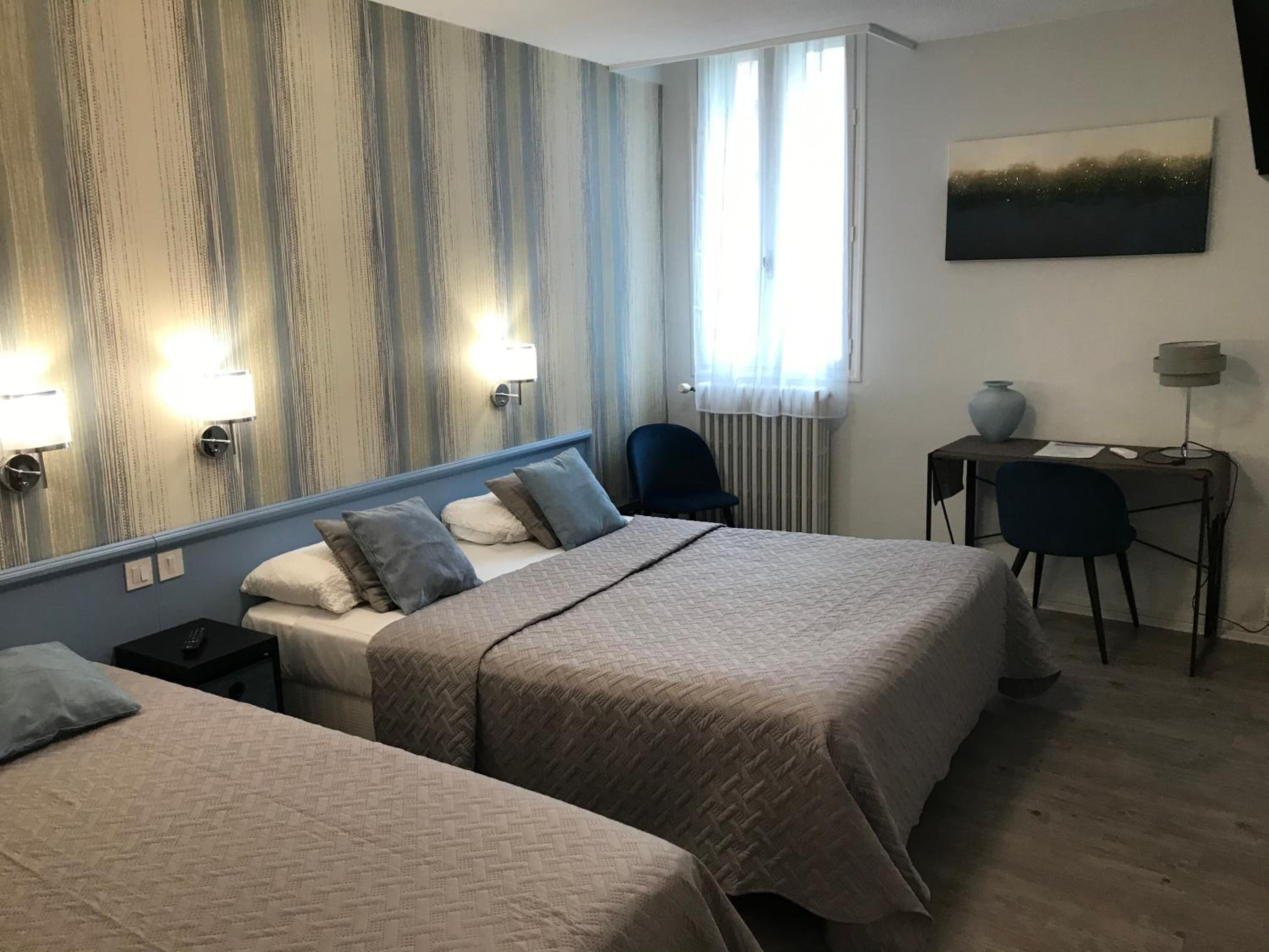 Une chambre d’hôtel avec deux lits, un bureau, une chaise et un tableau au mur.