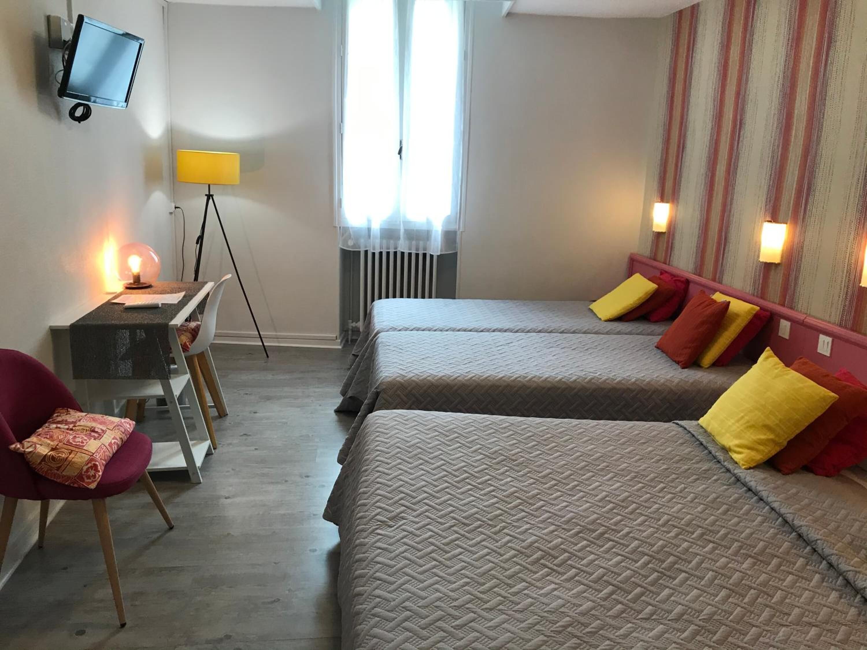 A hotel room with two beds, a desk with a chair, a television, and a window with curtains.