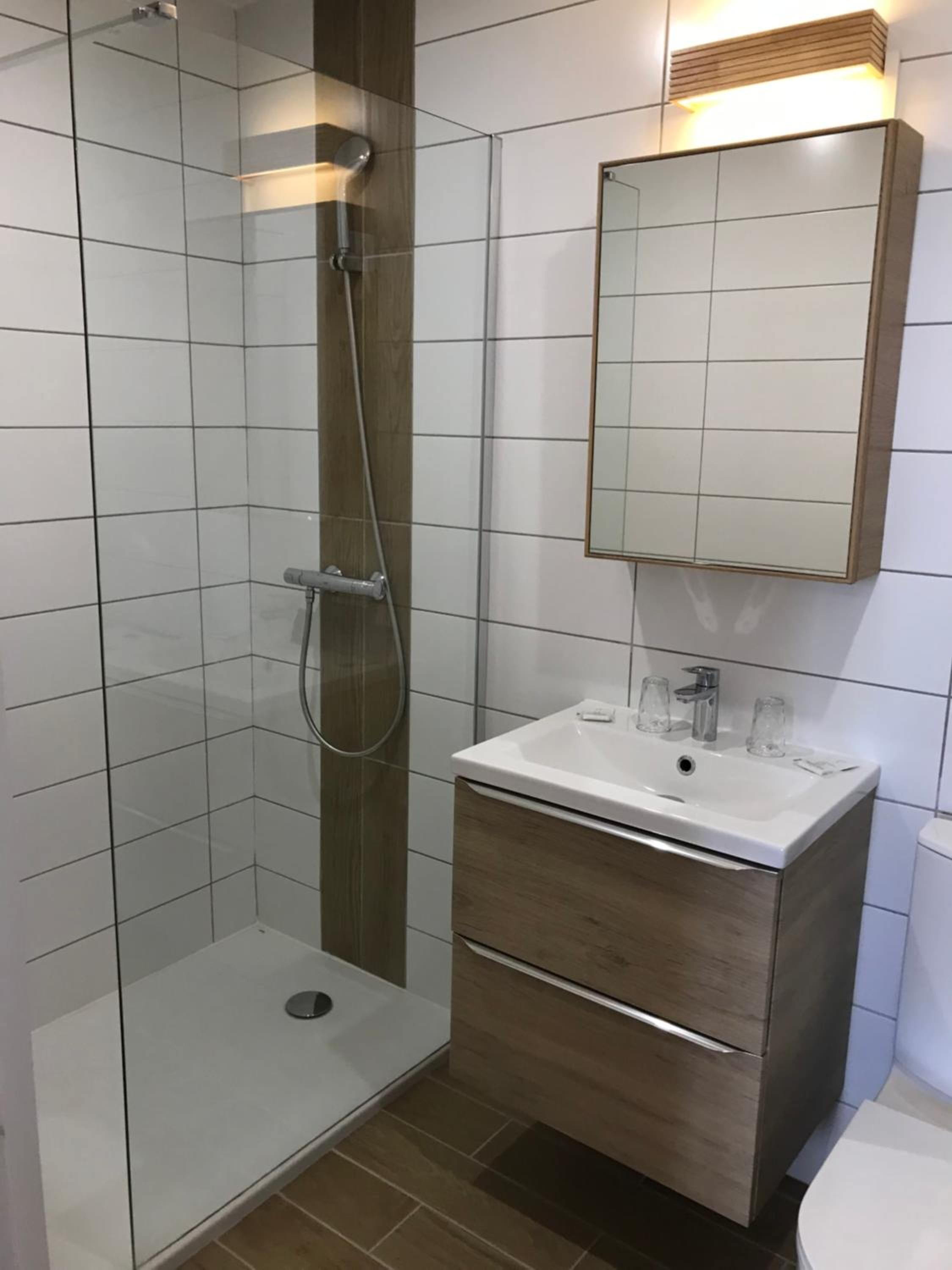 Een moderne badkamer met een douchecabine van glas, een houten wastafelmeubel met spiegel en een witte wasbak.