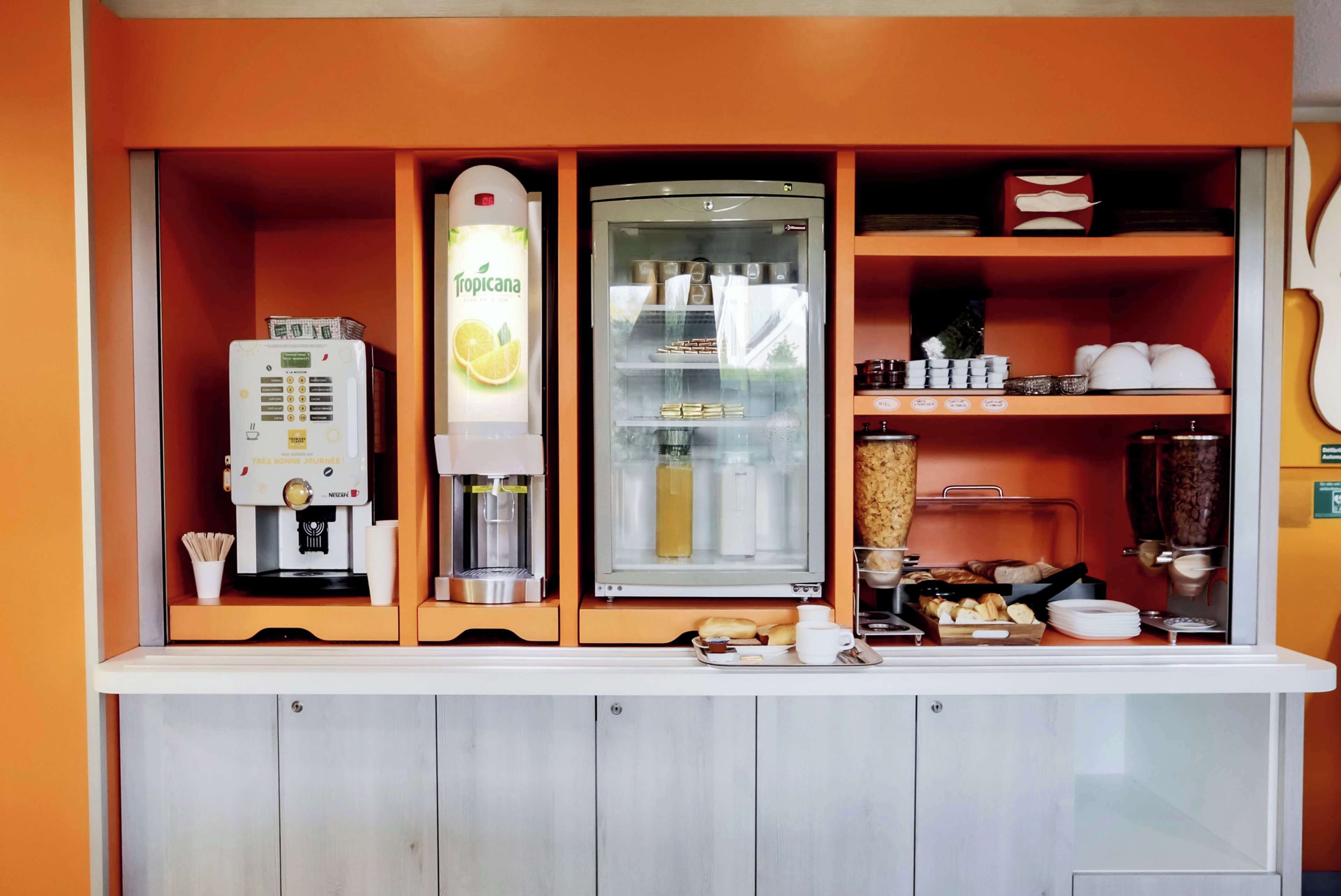 A self-service breakfast station with a coffee machine, a refrigerated drink dispenser, and a variety of food items.