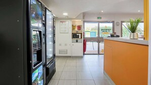 A hotel lobby with a vending machine, a microwave, a small kitchenette, and a reception desk.
