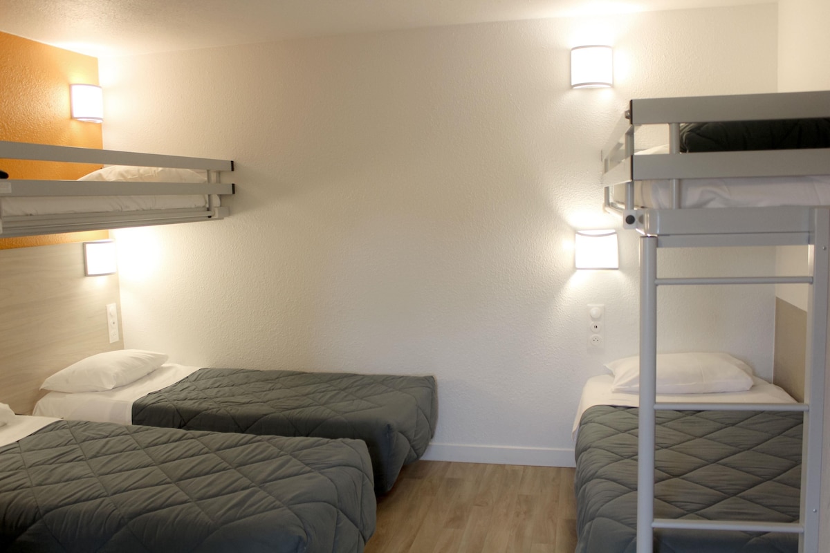 A room with bunk beds, two single beds, and bedside lamps.