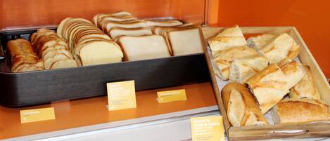 Una vitrina exhibe diferentes tipos de pan, como barras y pan de molde, con etiquetas que señalan su origen y variedad.