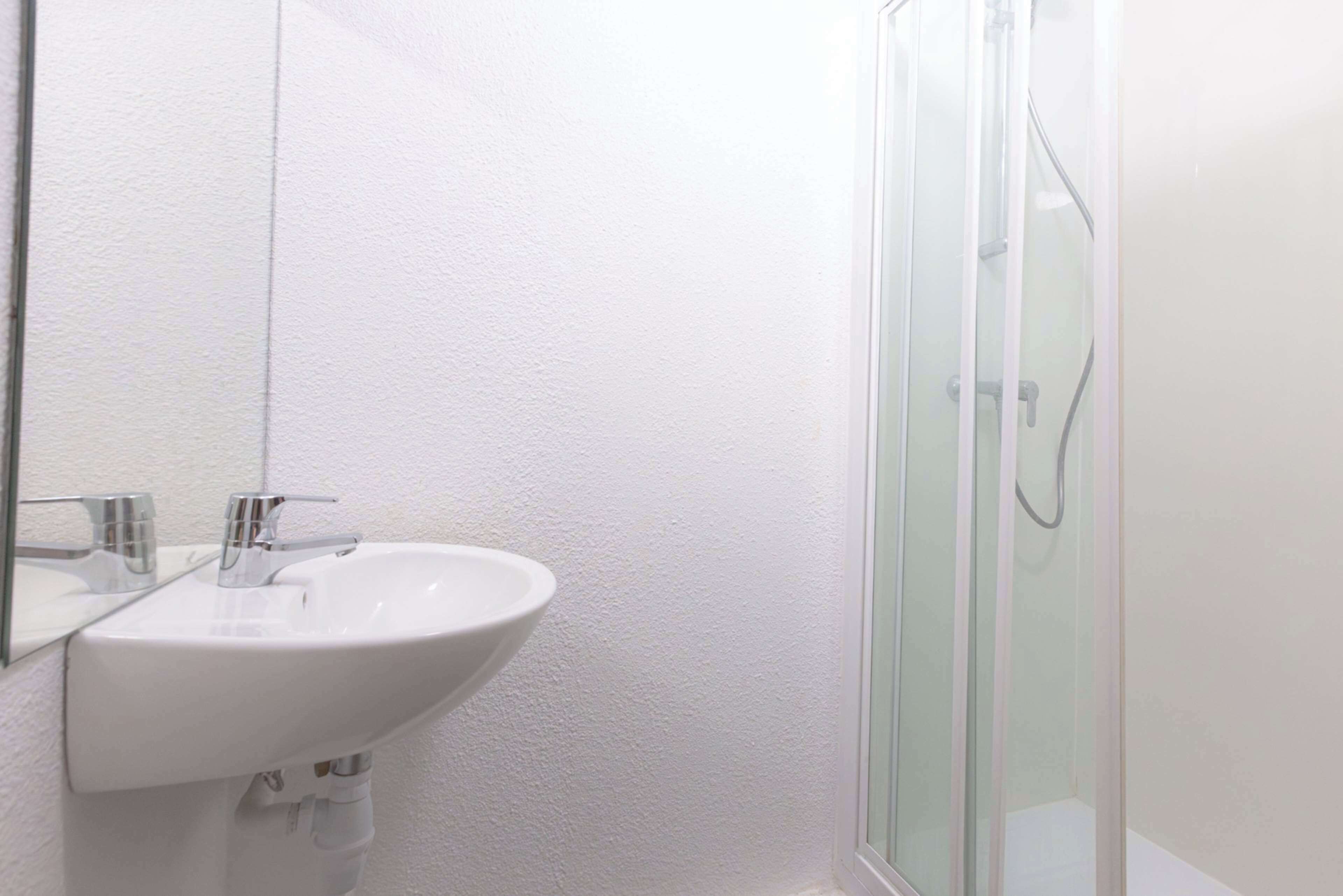 A bathroom with a white sink, a mirror, and a glass-enclosed shower.