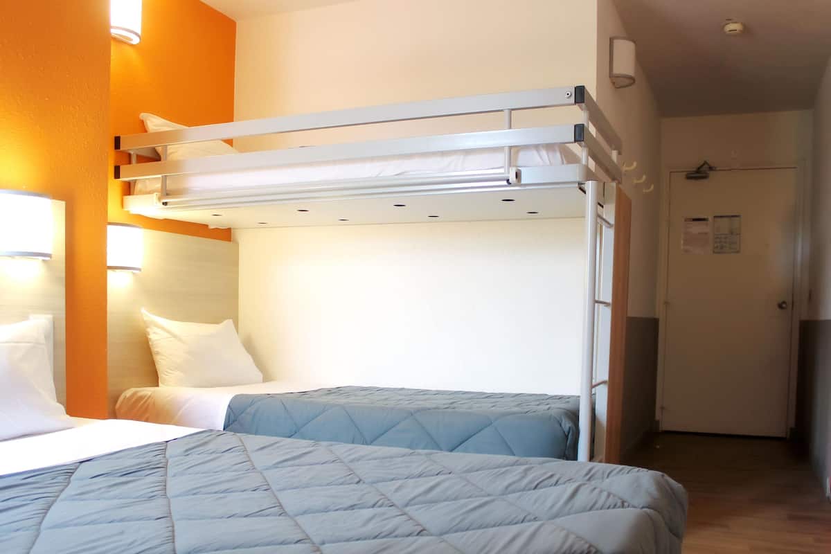 A room with two beds, one with a bunk bed on top, white bedding, and a blue quilted bedspread.