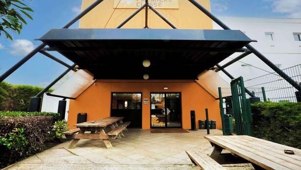 A hotel entrance with a covered patio area, outdoor seating, and a sign indicating the hotel name.