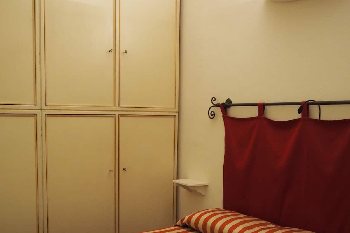 A bedroom with a striped bedspread, a red curtain, and a wardrobe with multiple doors.