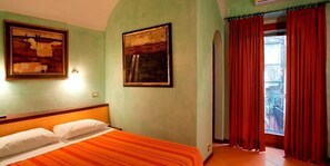 A room with a bed, two framed artworks on the wall, and a window with red curtains.