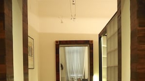 A hallway with wooden flooring leading to a room with a bed and a chair.