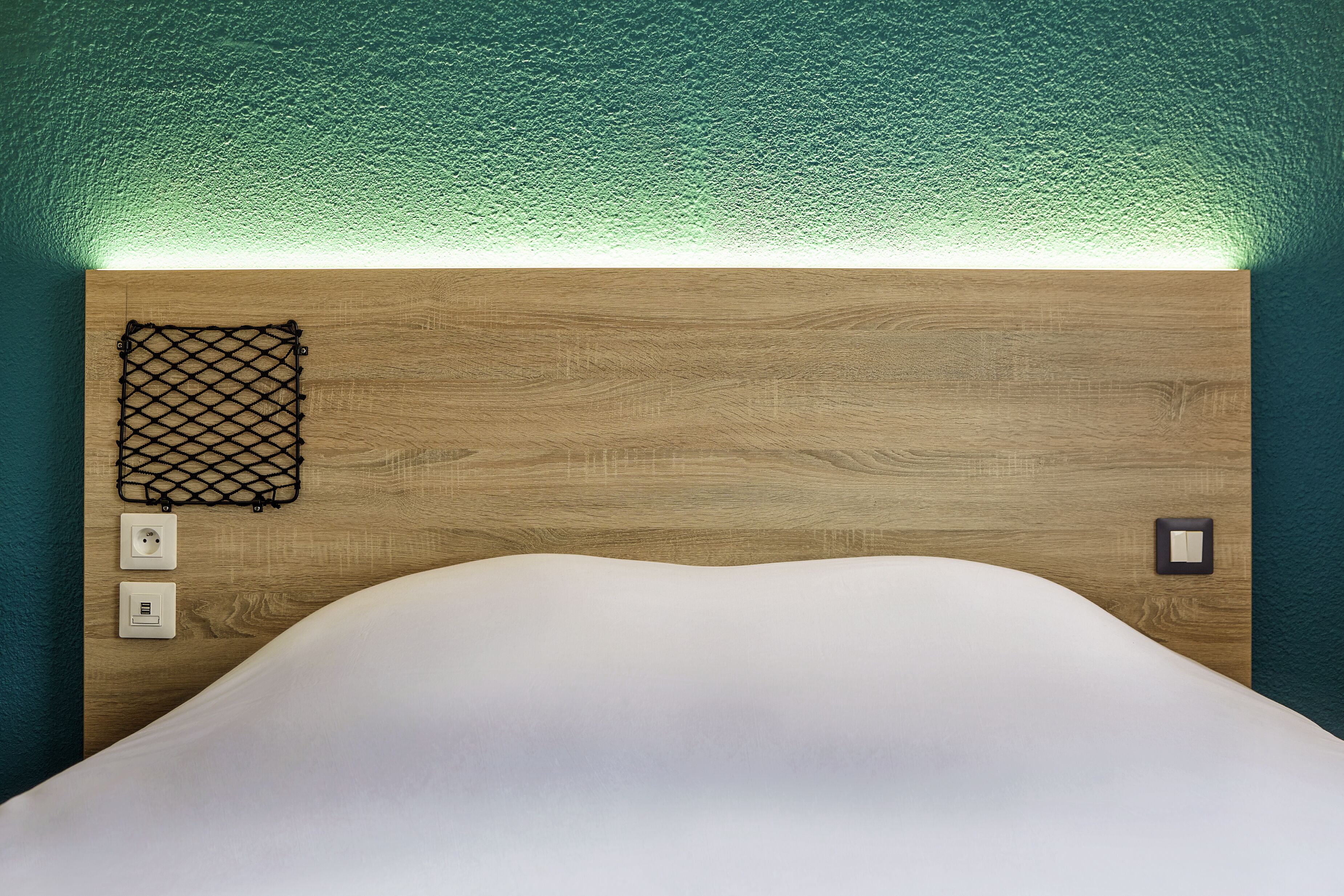 A neatly made bed with a white comforter and a wooden headboard.