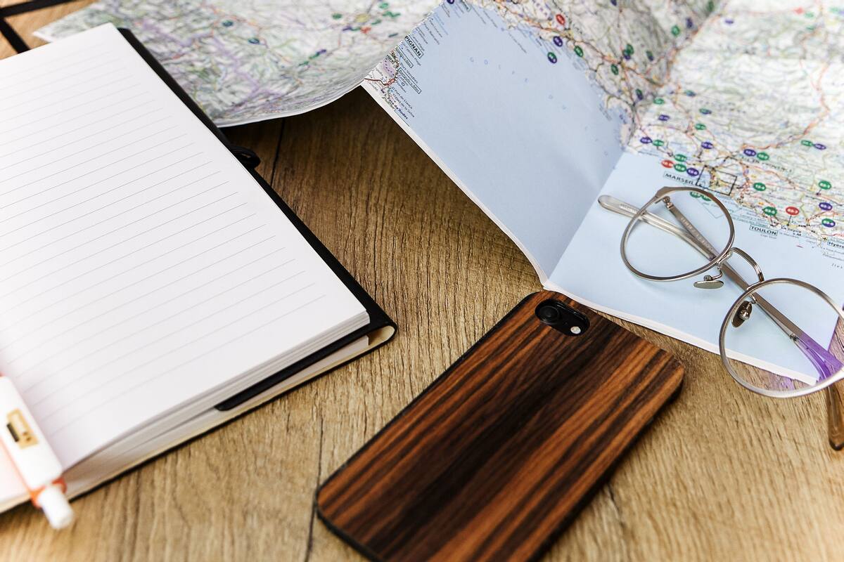 A notebook, a pair of glasses, and a map on a wooden surface.