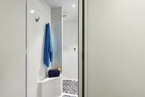 Un baño moderno con un box de ducha blanco, una toalla azul colgada en la pared y un estante pequeño con una bolsa.