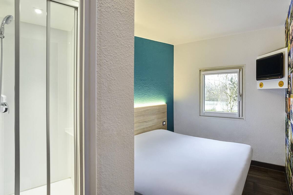 A hotel room with a bed, a shower, a window, and a TV.