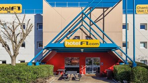 A hotel entrance with a prominent yellow sign, outdoor seating, and a staircase leading to the building. - hotelF1 Saint-Nazaire (Trignac)