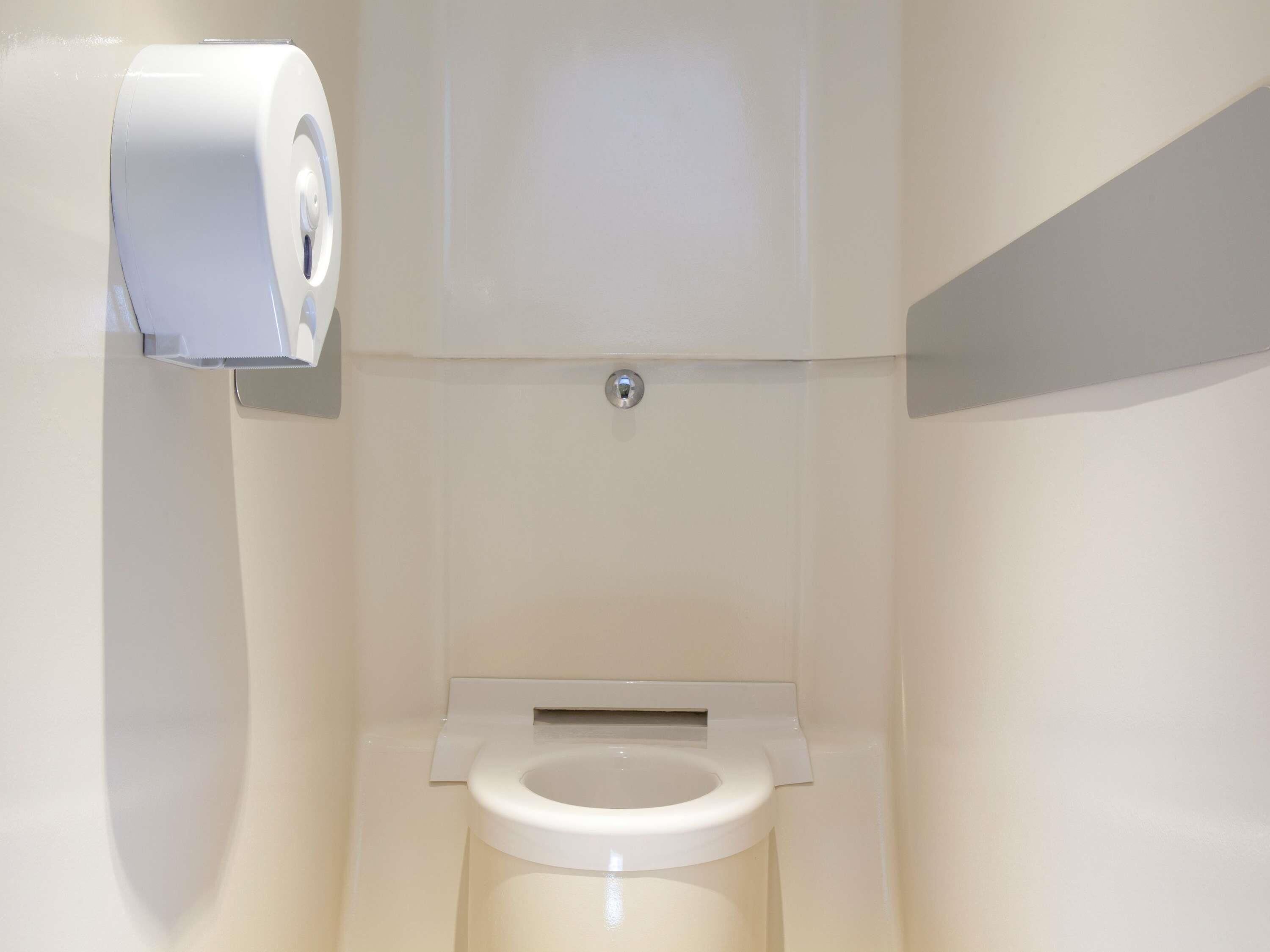 A toilet with a paper towel dispenser mounted on the wall.