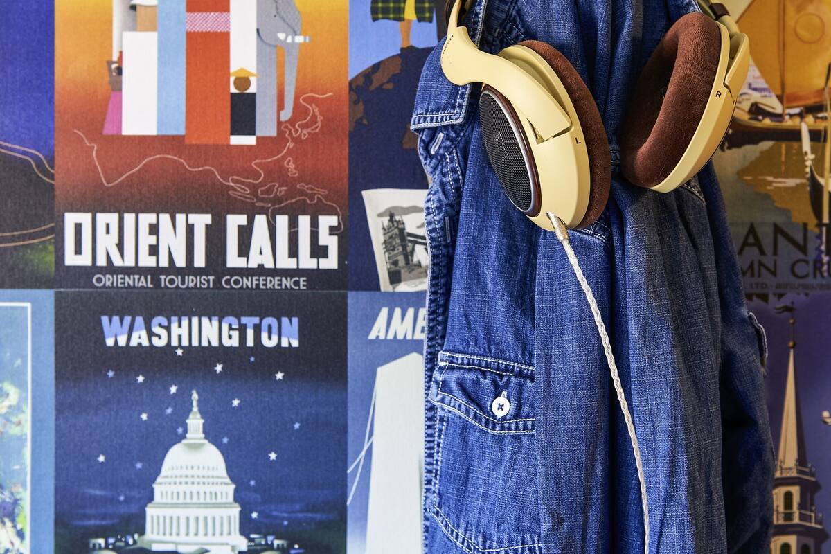 A denim jacket with headphones hanging on a wall with travel posters.