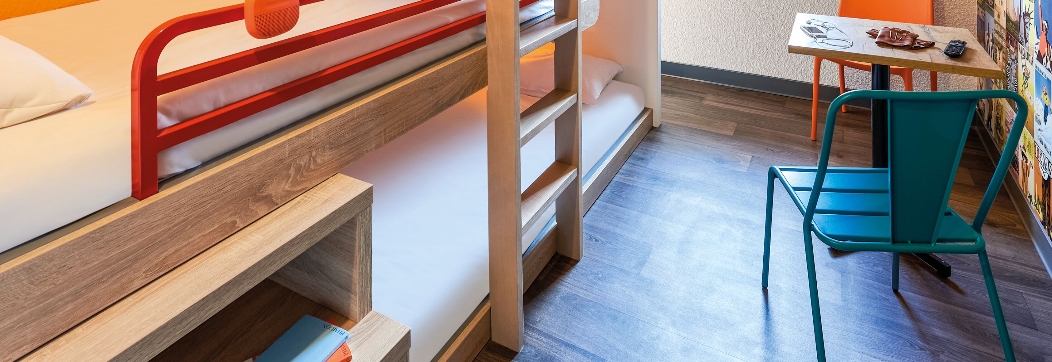 A compact room with a bunk bed, a small table with a chair, and a wall with posters.