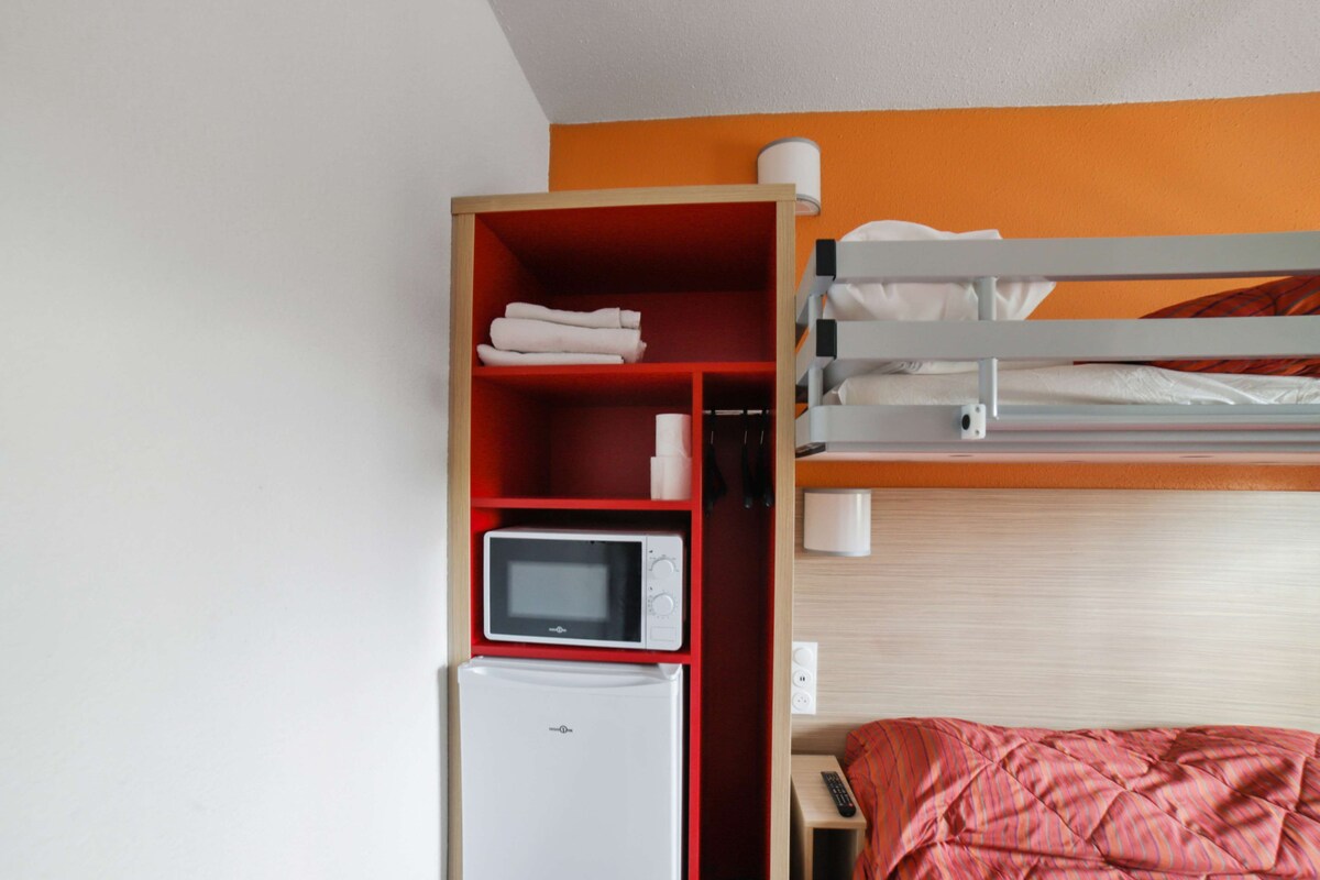 A bunk bed with a red shelf unit containing a microwave and a refrigerator.