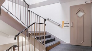 A staircase with metal railings, a door with a geometric design, and directional signs indicating room numbers. - Premiere Classe Angers Est - St Barthelemy D'Anjou (Saint-Barthelemy-d'Anjou)