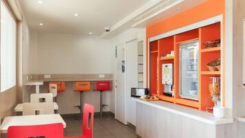 A modern cafe with white and orange decor, featuring a counter with a coffee machine and a refrigerator.