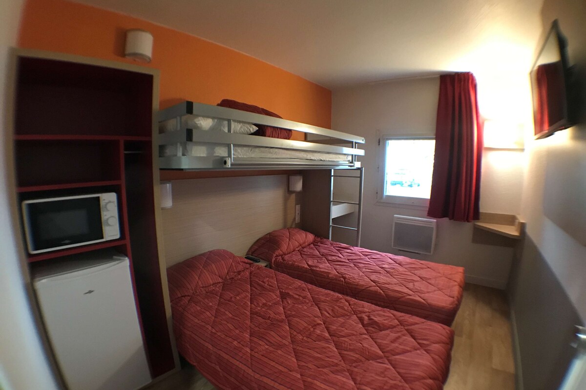 Une petite chambre avec des lits superposés, un four à micro-ondes, un petit réfrigérateur et une fenêtre avec des rideaux.