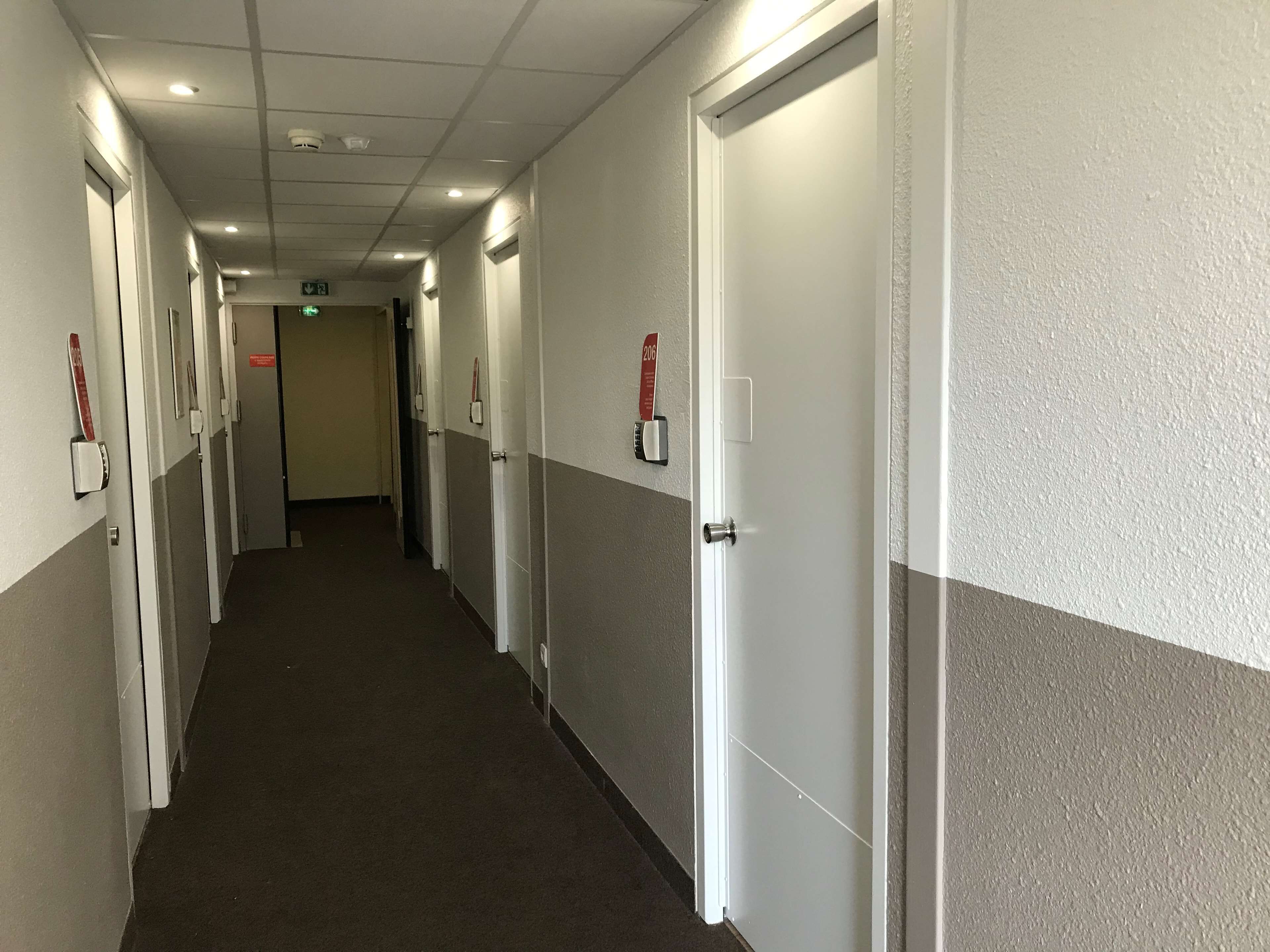 A hotel corridor with doors, a carpeted floor, and a ceiling with recessed lighting.