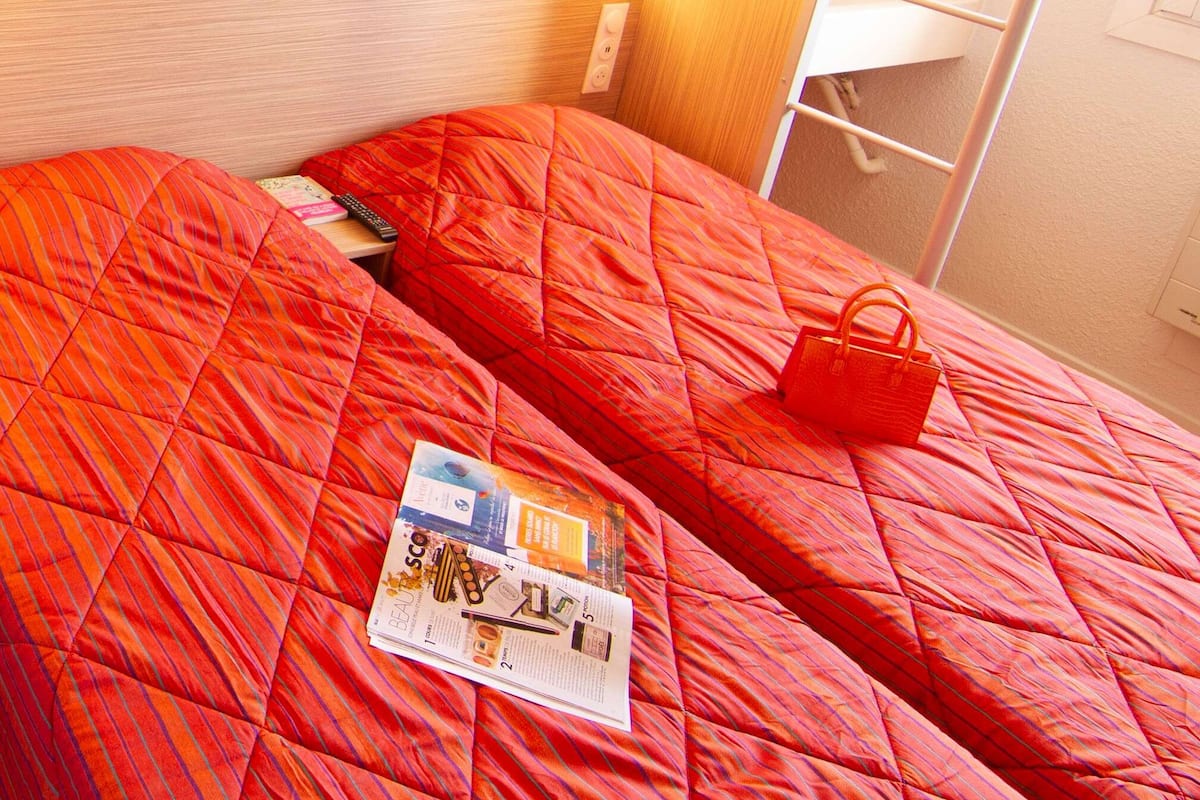 Un lit superposé avec une couette matelassée rouge et un magazine sur le lit du bas.