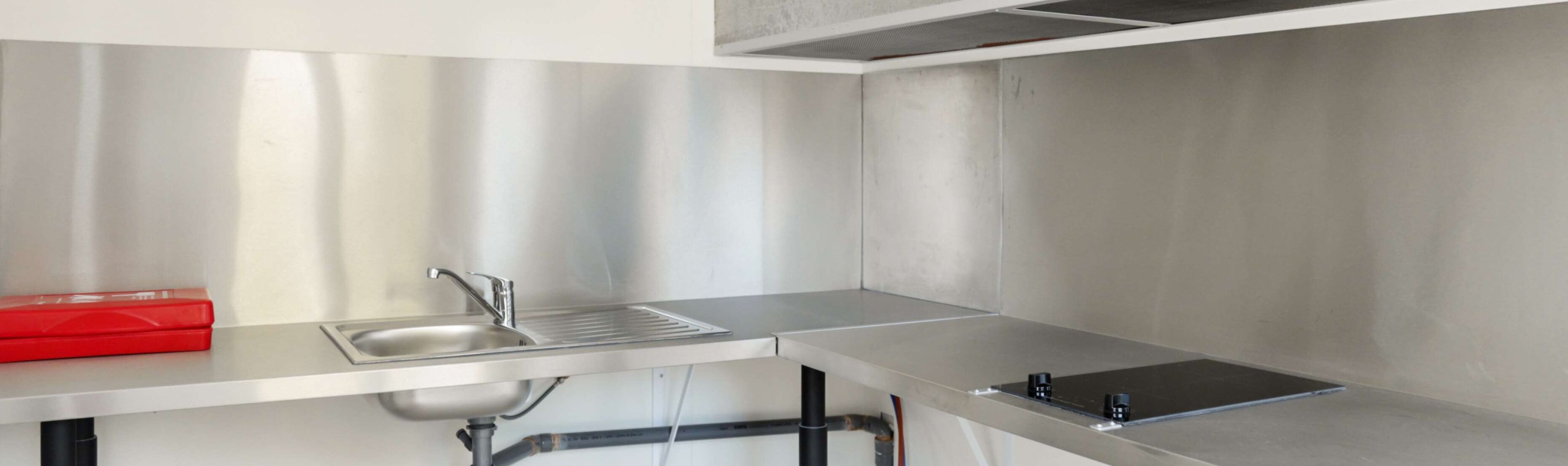 A modern kitchen with stainless steel countertops, a sink, and a red box on the left.
